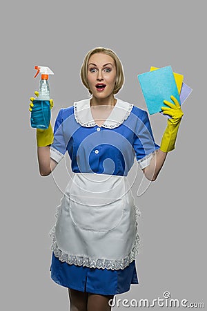 Happy shocked maid in uniform holding rags and detergent. Stock Photo