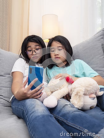 Happy siblings children sitting on sofa in living room speak with parent on mobile phone together, smiling elder girl showing cute Stock Photo