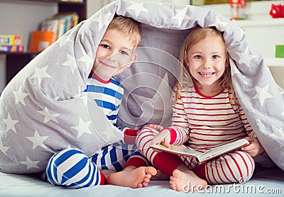 Happy siblings reading book under cover Stock Photo