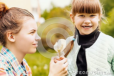 Happy sisters hold dandelions together in the park in the spring. Caring, loving older sister gives wildflowers to her younger Stock Photo