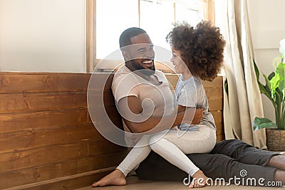 Happy smiling african american man sitting on floor, holding daughter. Stock Photo