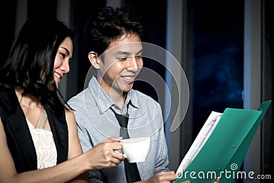 Happy smiling Asian business man and woman working together, looking work file and having discussion, employee working hard Stock Photo