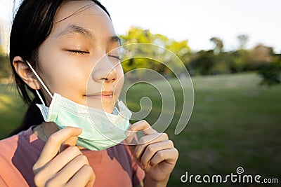 Happy smiling asian child girl is standing,taking off mask in green nature,breathe deep,woman enjoy breathing fresh air with Stock Photo