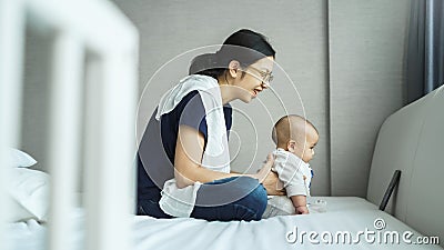 Smiling Asian Young mother and adorable newborn baby doing online video chat with family on smartphone Stock Photo