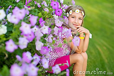 Happy smiling blond model child girl sitting on grass in flowers Stock Photo