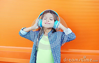 Happy smiling child enjoys listens to music in headphones over colorful orange Stock Photo