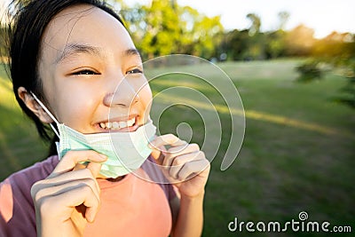 Happy smiling child girl is standing,taking off mask in green nature,breathe deep,woman enjoy breathing fresh air,relaxing in park Stock Photo