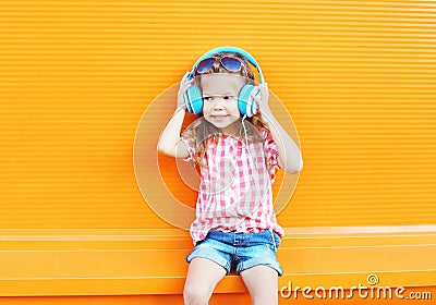 Happy smiling child listens to music in headphones over colorful orange Stock Photo