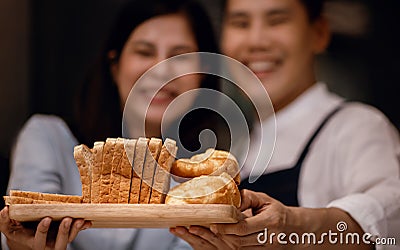 Happy Smiling Couple Presenting some Fresh Bread on Wooden Tray. Bake at Home. Closeup Stock Photo