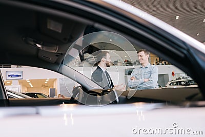 Happy smiling customer and friendly salesman wearing business suit standing near expensive car Stock Photo