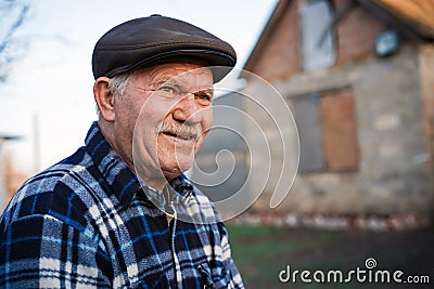 Happy smiling elder senior man portrait with a mustache in a cap on the background of a brick house in a Russian village Stock Photo