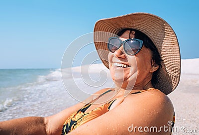 Happy smiling Elderly womanr woman in sunglasses and big hat takes sun bath on seaside Stock Photo