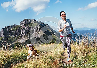Happy smiling female jogging by the mounting range path with her beagle dog. Canicross running healthy lifestyle concept image Stock Photo