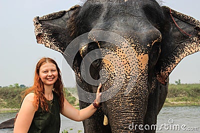 Happy smiling girl traveler with red hair in a green t-shirt holding a big elephant Stock Photo