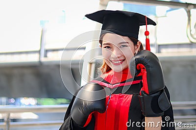 Happy smiling graduated woman student warming square academic hat cap with red boxing gloves or mitt punch, the metaphors about Stock Photo