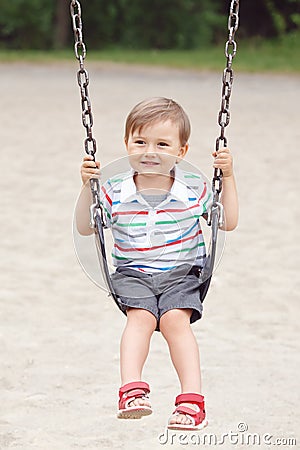 Happy smiling little boy toddler in tshirt and jeans shorts on swing on backyard playground outside Stock Photo