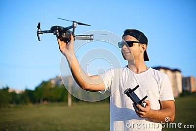 Happy smiling man holds small compact drone and remote controller in his hands. Pilot launches quadcopter from his palm Stock Photo