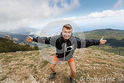 Happy smiling man stands on a top of the mountain with open hands and strong expession looking at camera with summer Stock Photo