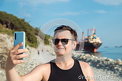 Happy smiling man taking selfie with phone outdoors against sunken cargo ship. 32 years old Caucasian tourist man. Close-up summer Stock Photo