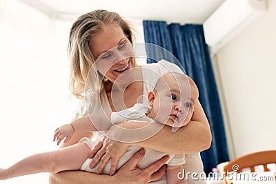 Happy smiling mother holds and hugs her baby in a bright room. Harmonious family, happy motherhood and childhood. Stock Photo