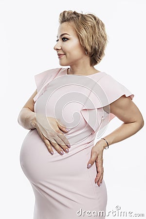 Happy smiling pregnant blonde woman stands and touches big belly. Waiting for the birth of a baby. White background. Vertical Stock Photo