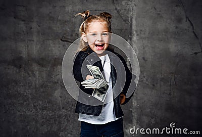 Happy smiling rich kid girl in leather jacket and white t-shirt is handing giving a bundle of money cash dollars Stock Photo