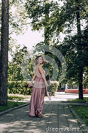 Happy and smiling woman with bouquet of flowers in a pink wedding dress and wedding ring. Running Bride, Bridesmaid. City park Stock Photo