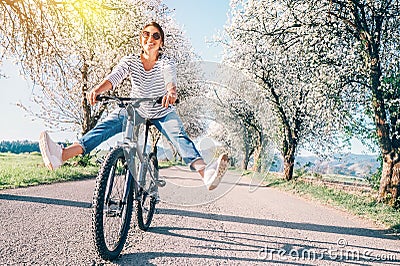 Happy smiling woman cheerfully spreads legs on bicycle on the country road under blossom trees. Spring is comming concept image Stock Photo