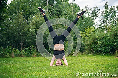 Happy smiling woman enjoy gymnastic yoga doing headstand asana on a forest meadow. Stock Photo