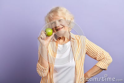 Happy smiling woman in her sixties holding green apple and smiling at camera. Stock Photo