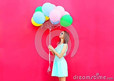 Happy smiling woman is looking on an air colorful balloons having fun over pink background Stock Photo