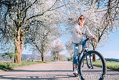 Happy smiling woman rides a bicycle on the country road under blossom trees. Spring is comming concept image Stock Photo