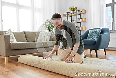 happy smiling young man unfolding carpet at home Stock Photo