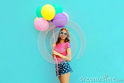 Happy smiling young woman with bunch of balloons having fun wearing a shorts and pink t-shirt on blue wall Stock Photo