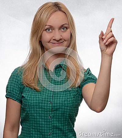 Happy and smiling young woman in casual green shirt pointing up and looking straight into camera Stock Photo