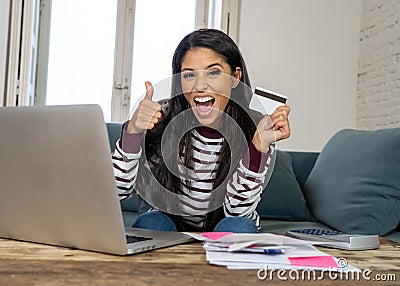 Happy smiling young woman making online payments bills using laptop and credit card and thumb up Stock Photo