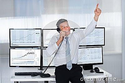 Happy stock trader pointing upwards while using telephone Stock Photo