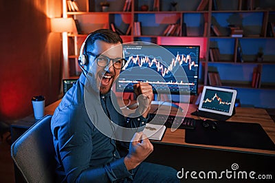 Happy stock trader is working by pc indoors and celebrating success. Conception of exchange and money Stock Photo