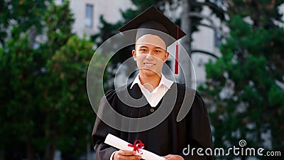 Happy student graduate posing in front of the camera with his diploma in the graduation suit and cap Stock Photo