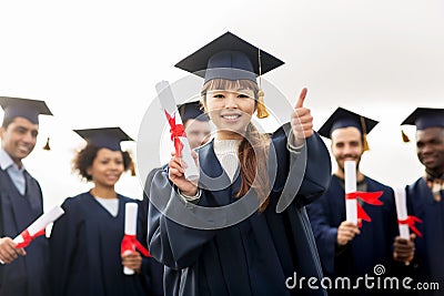 Happy students with diplomas showing thumbs up Stock Photo