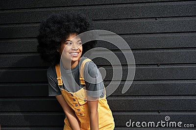 Happy stylish African lady with afro hair looking away stand against black wall. Stock Photo