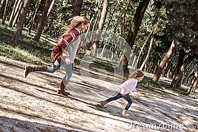 Happy, stylish little curly girl is running with her beautiful mother in forest Stock Photo