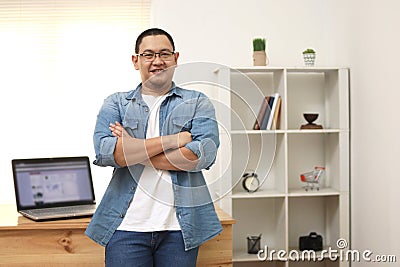 Happy succesful young Asian entrepreneur smiling at camera confidently in his home office studio Stock Photo