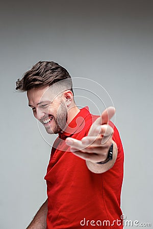Happy embarrassed successful laughing young man holds out hand to camera, studio ad portrait on gray with copy space Stock Photo
