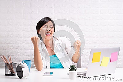 Happy successful woman with raised hands sitting at home office working using laptop Stock Photo