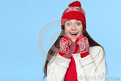 Happy surprised woman looking sideways in excitement. Christmas girl wearing knitted warm hat and mittens, isolated on blue Stock Photo
