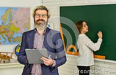 Happy teacher and child in classroom. change of duties. bearded man make notes in clipboard. little girl write answer on Stock Photo