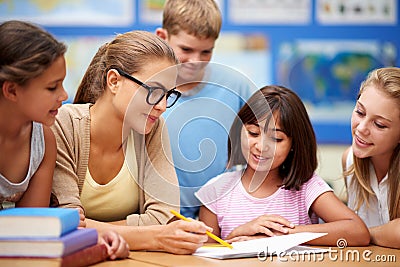 Happy teacher, students and writing for education, learning or tutoring in classroom at school. Woman, mentor or Stock Photo