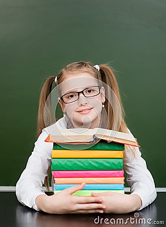 Happy teen girl with pile books near empty green chalkboard Stock Photo