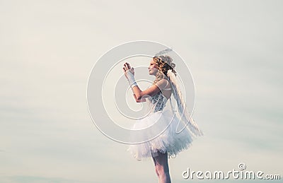 Happy teenage angel girl pray. Child with angelic character. Girl dressed as an angel on a light heaven background Stock Photo